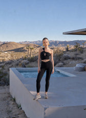 Person in black athletic wear standing by a pool with desert landscape and mountains in the background