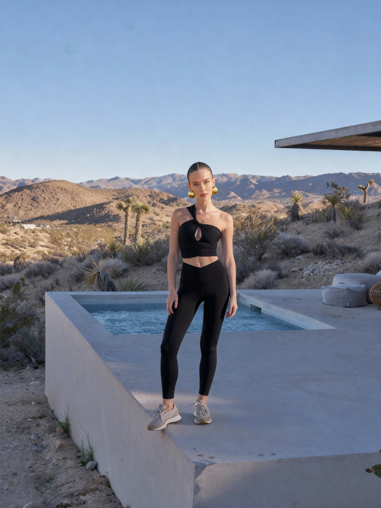 Person in black athletic wear standing by a pool with desert landscape and mountains in the background