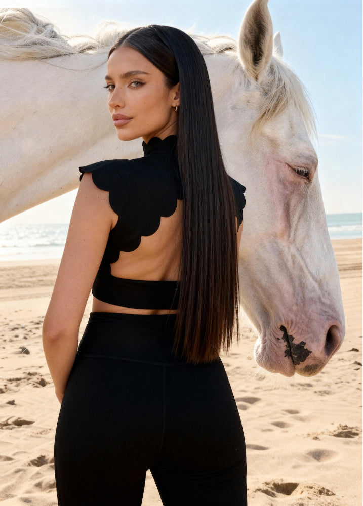 Woman in black outfit standing next to a white horse on a beach