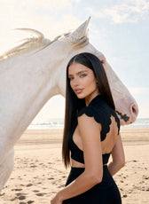 Woman in a black dress standing next to a white horse on a beach