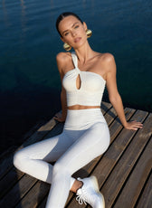 Woman in white outfit sitting on a wooden dock by water