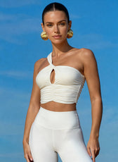 Woman wearing a white one-shoulder top and white pants against a blue sky.