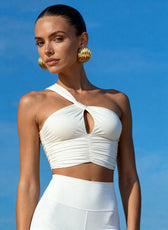 Woman wearing a white halter top and white pants against a blue sky.