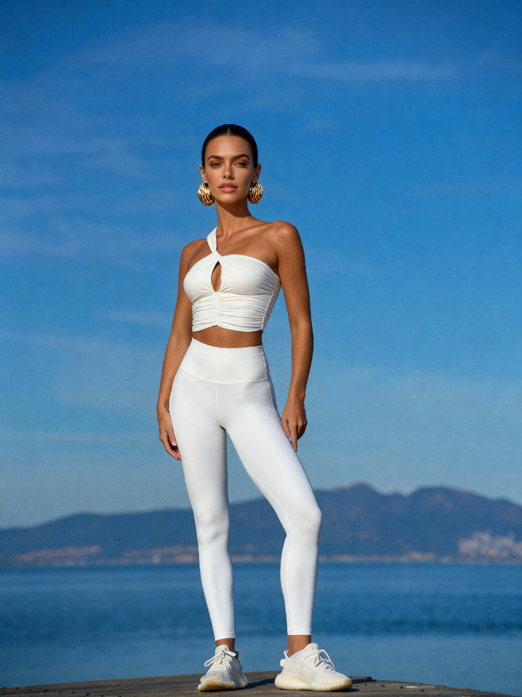 Woman in a white outfit standing on a dock with a blue sky and mountains in the background