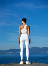 Person wearing a white outfit standing by a body of water with mountains in the background