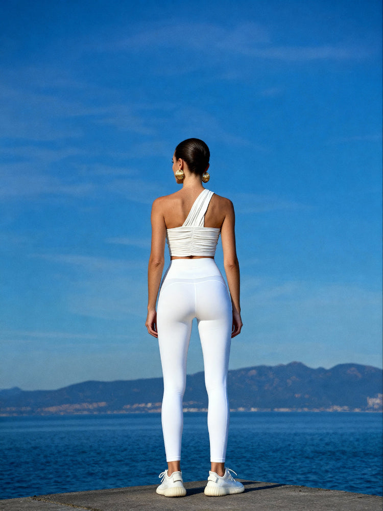 Person wearing a white outfit standing by a body of water with mountains in the background