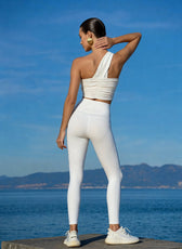 Woman in white athletic wear standing by a body of water with mountains in the background