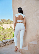 Woman in a white outfit standing against a stone wall with a scenic background