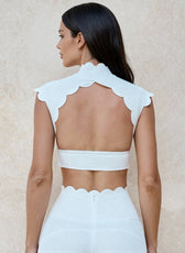 Woman wearing a white outfit with scalloped edges on a beige background